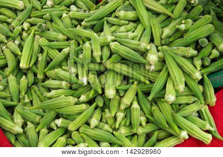 Bright green finger okra pouring from bucket onto red cloth display