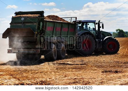 tractor with trailer full of organic fertilizer or manure to the stubble field on a sunny summer day
