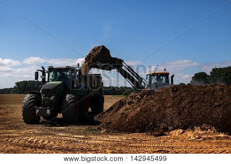 fertilize the field excavator with shovel fills organic fertilizer or manure in the trailer of a tractor blue sky copy space