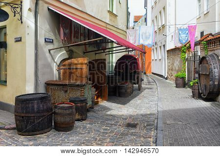 Old barrels and a cart on the street with stylized medieval flags on the facades in the historic center of Riga
