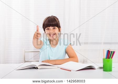 Cute little girl is showing thumbs up while she is doing her homework.