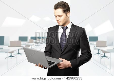 Handsome businessman looking at laptop screen in coworking office interior