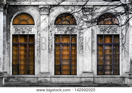 Facade of old abandoned building with three large arched windows of orange glass. Monochrome background