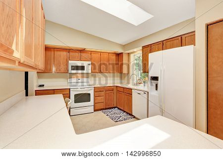 Kicthen In White Tones With Wooden Cabinets And White Counter Top.