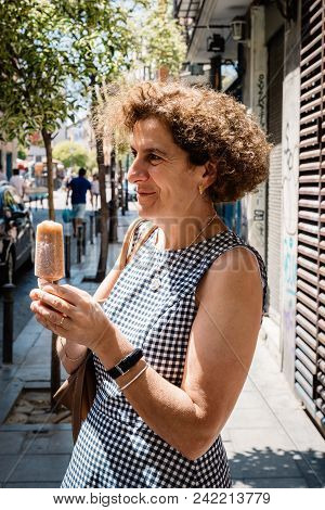 Elegant Woman Eating Ice Cream On The Street. She Is Smiling And Having A Good Time