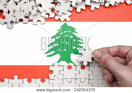 Lebanon Flag  Is Depicted On A Table On Which The Human Hand Folds A Puzzle Of White Color.