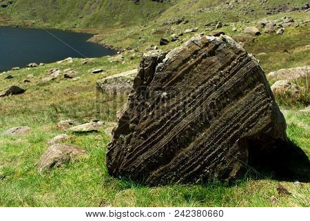 Layering within a lump of sedimentary rock resting on a hillside above a reservoir in the Lake District, UK.