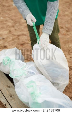 Worker in gloves binding big sacks with litter by green rubber band while preparing them for utilization