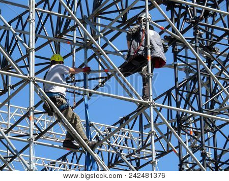 Construction Workers On Scaffolding. Steeplejacks On The Background Of Clear Blue Sky