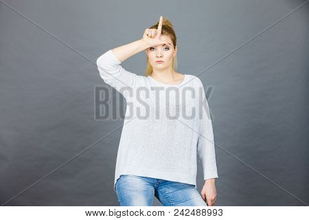 Woman Showing Mean Sign, Lame Or Loser Gesture With L Fingers On Forehead, Grey Background.