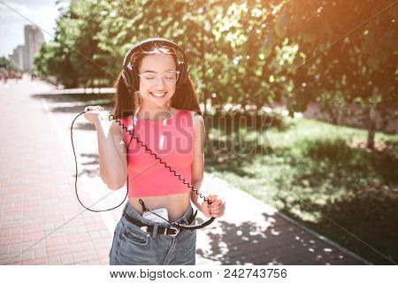 Attractive Melomaniac Is Walking Down The Road And Smiling. She Is Looking Down And Enjoying The Mom