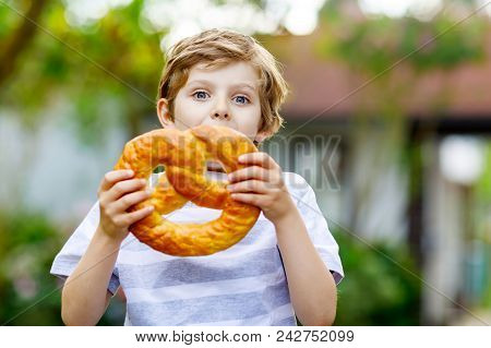 Adorable Little Kid Boy Eating Huge Big Bavarian German Pretzel. Happy Blond Child Enjoying Tasteful