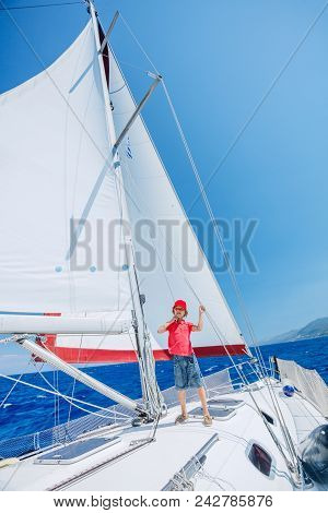 Cute Boy On Board Of Sailing Yacht On Summer Cruise. Travel Adventure, Yachting With Child On Family
