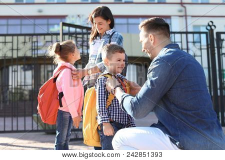 Young Parents Saying Goodbye To Their Little Children Near School