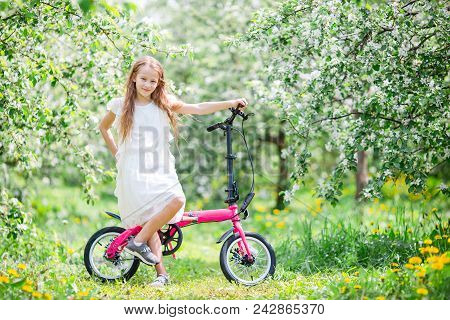 Adorable Girl Riding A Bike At Beautiful Summer Day Outdoors In Blooming Park