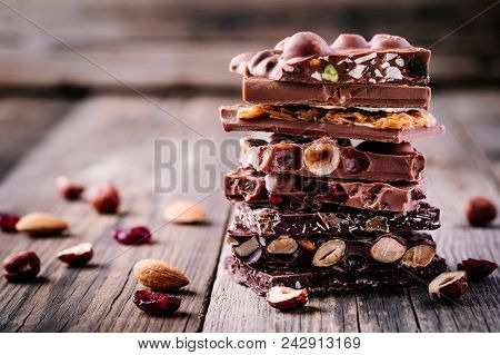 Stack Of  Milk And Dark Chocolate With Nuts, Caramel And Fruits And Berries On Wooden Background.