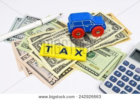 A Blue Toy Car, Pen, Calculator And The Word Tax, Sits On A Bed Of Dollar Currency Notes. A Financia