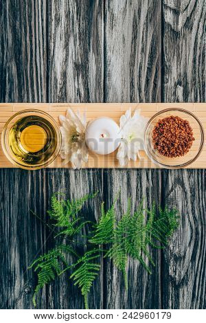 Top View Of Arranged Oil, Scrab, Candle And Chrysanthemum Flowers For Spa And Massage On Wooden Tabl