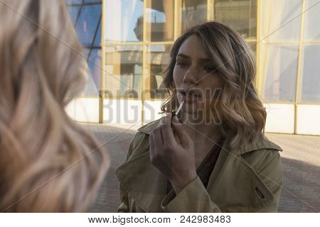 Attractive Young Caucasian Blonde Woman In Trench Walking In City Mirrors With Vintage Suitcase