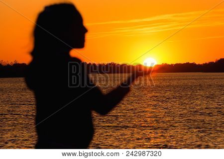 Silhouette Of A Girl On The Background Of The Evening Sun Red Sunset, Keeps The Sun In His Hand