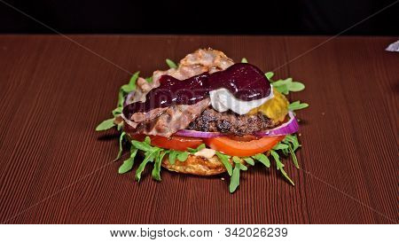 Craft Burger Is Cooking On Black Background. Consist: Sauce, Arugula, Tomato, Onion, Bacon, Currant 