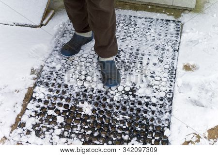 A Man Wearing Goloshes And Wool Socks Standing On The Doormat Covered With Snow