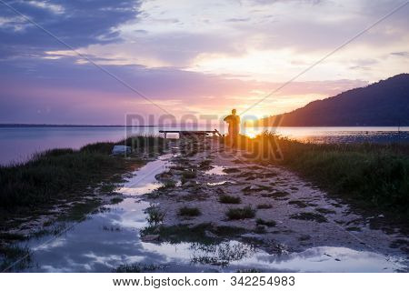 Silhouette Of Woman Walking Towards Orange Sunset On Dramatic Purple Blue Sky Along Lake Itza, El Re