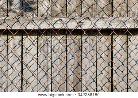 A Weathered Old Gray Wooden Fence With A Horizontal Bar Nailed By Rusty Nails Stands Behind A Rusty 
