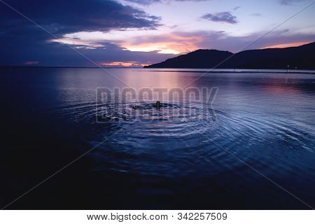 Swimming Person At Orange Sunset On Dramatic Purple Blue Sky Along Lake Itza, El Remate, Peten, Guat