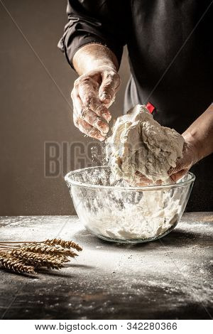 A Cook In Black Knead The Dough In A Glass Bowll Bowl For Cooking Bread In The Kitchen. Yeast Dough 