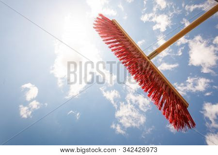 Broom Red Sweeping Brush Against Blue And White Cloudy Sky. Household Obejcts Concept.