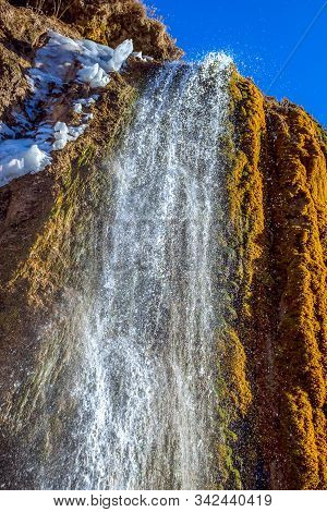Spring Waterfall In The Mountains With The Remains Of Old Snow.