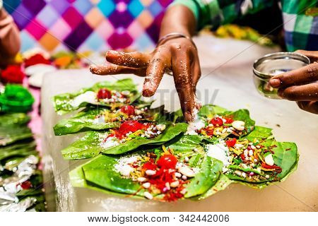 A Hand Sprinkling Pan Masala Garnish And Cherry On Betel Leaf During Preparation Of Banarasi Pan.