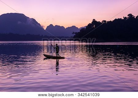 Man Stand Paddling On His Kayak At Ratchaprapa Dam, Or Known As Cheow Lan Dam, During Sunrise