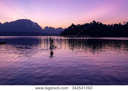 Man Stand Paddling On His Kayak At Ratchaprapa Dam, Or Known As Cheow Lan Dam, During Sunrise