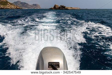 Stern Wave Of A Motor Boat With The Motor In Foreground And The Rocky Coastline On The Eastside Of G