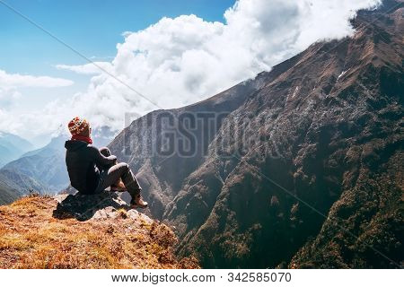 Young Female Hiker Backpacker Sitting On The Peak Edge And Enjoying Mountains View Valley During Hig