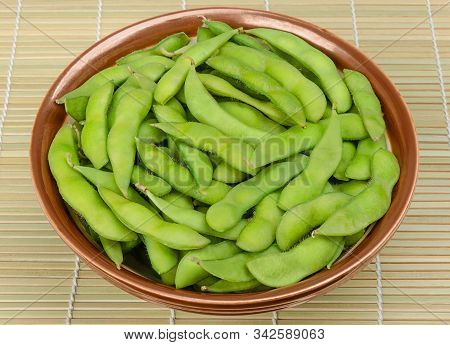 Boiled Edamame In A Brown Bowl On A Bamboo Mat. Green Soybeans, Also Maodou, Cooked In Saltwater. A 