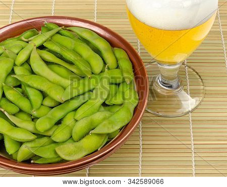 Boiled Edamame In A Bowl With A Glass Of Beer On Bamboo Mat. Green Soybeans, Maodou, Cooked In Saltw