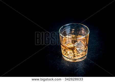 Whisky, Whiskey, Bourbon Or Cognac With Ice Cudes On Black Stone Table