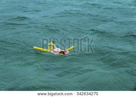 Young Female Caucasian Child Snorkeling In The Waters Over A Shallow Coral Reef Using A Noodle For B
