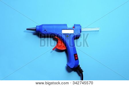 Electric Blue Hot Glue Gun With Glue Stick On A Blue Background