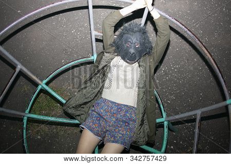 Funny Caucasian Girl Wearing Gorilla Mask, Coat And Shorts Lying On Metal Construction Of Children P