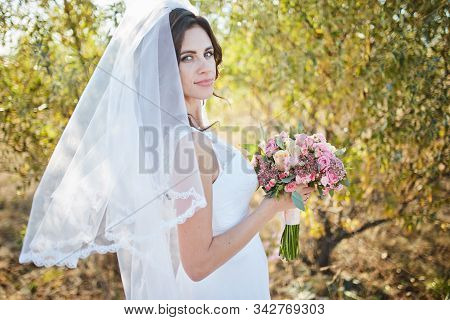 Beautiful Smiling Bride Wearing A Natural Flower Wreath And Standing In The Golden Summer Fields Wit