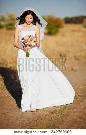 Beautiful Smiling Bride Wearing A Natural Flower Wreath And Standing In The Golden Summer Fields Wit
