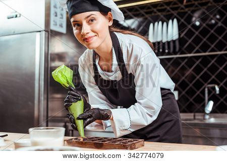 Selective Focus Of Happy Chocolatier In Black Latex Gloves Holding Pastry Bag Near Chocolate Molds
