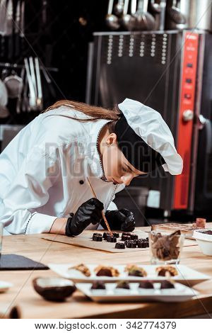 Selective Focus Of Attractive Chocolatier Holding Brush With Gold Powder Near Prepared Chocolate Can