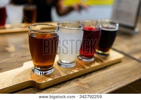 Flight Of Craft Four Of Different Beers Glasses, Brown Black White And Red Beer On A Wooden Tray Dur