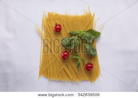 Italian Pasta Concept. A Pile Of Unboiled Spaghetti, Basil Leaves And Cherry Tomatoes Close-up.