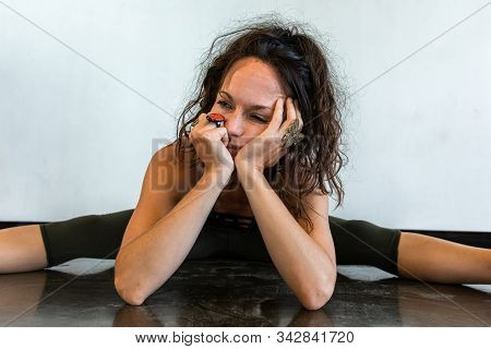 Portrait Of A Tired Caucasian Woman With Messy Brown Hair In A Leg Split Seated Pose At The End Of V